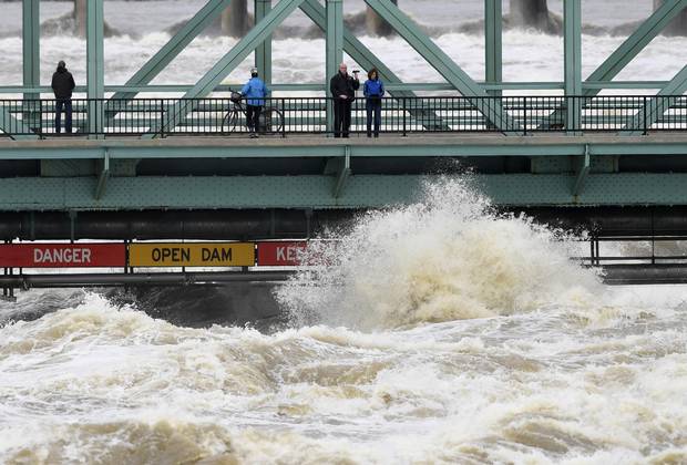 Water crashes against signage and pipes underneath the Chaudiere Bridge, close to onlookers, in Ottawa as water levels on the Ottawa River run high, on Tuesday, May 9, 2017.