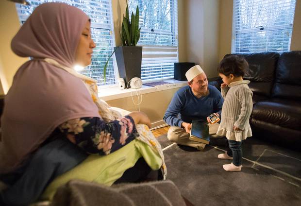 David Bathurst reads the Quran near his wife Kelly and his child Nura, 2, in their home in Burnaby.