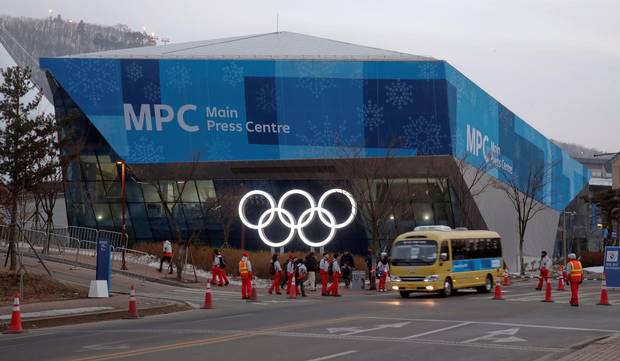 A shuttle bus drives past volunteers in front of the Main Press Center at the Alpensia mountain resort in Pyeongchang on Feb. 18, 2018.