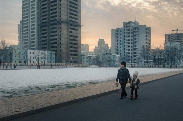Winter sun low on the horizon, a mother and daughter walk to school through an inner-city neighbourhood as schoolchildren play basketball in the distance. Although the skeletons of stalled construction projects are a common sight throughout Pyongyang, true urban blight here is rare, with pride of presentation an important part of city life.