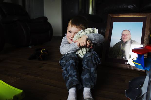 Casey Smith hugs his blanket in front of a photo of his late father, Cpl. Scott Smith.