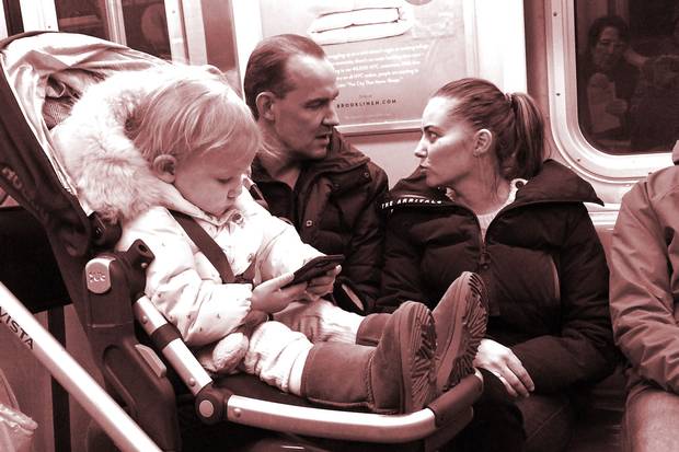 A baby plays with a mobile phone on a New York subway. Recent research posits a link between babies’ smartphone use and how they develop eye contact with their parents, which can have an impact on brain development.