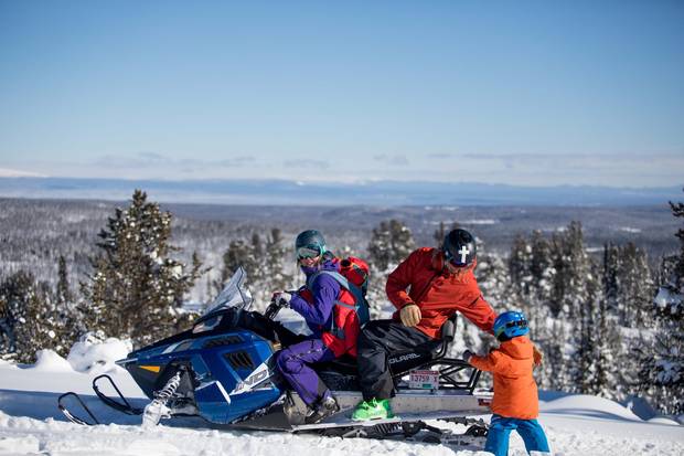 Tessa Treadway gets ready to snowmobile with her son Raffi on her back as her husband Dave Treadway loads up their other son Kasper near Tweedsmuir Ski Club.