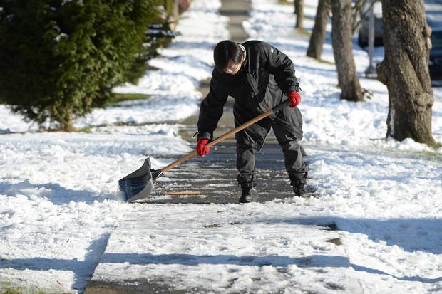 A man clears ice off the sidewalk in front of his house in Vancouver on Jan. 3, 2017. An unusual bout of snowy winter weather has confounded residents of southern British Columbia, resulting in unplowed streets and icy sidewalks.