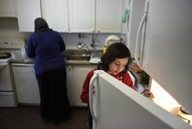 Rama Al Dibel, 9, grabs something from the fridge while helping her mom, Abir Abdel Al Kader, prepare a meal.