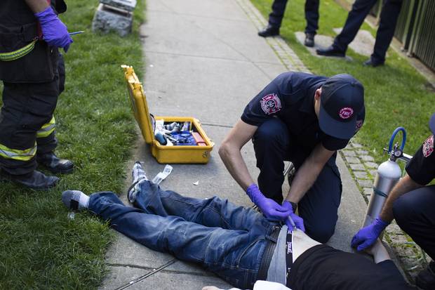 Firefighter Brandon Davies, middle, gives an overdose victim an injection. 