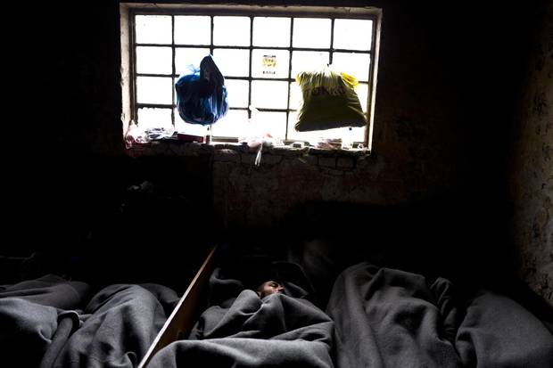 A migrant sleeps on the ground under a window of an abandoned warehouse in Belgrade.