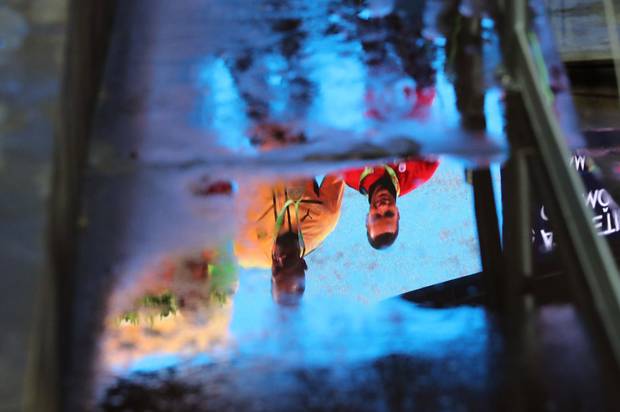A large screen showing the medal ceremony of the men's 100-meters awarding Jamaica's Usain Bolt the gold medal, United States' Justin Gatlin the silver medal and Canada's Andre De Grasse the bronze medal, is reflected in a puddle on the track during the athletics competitions of the 2016 Summer Olympics at the Olympic stadium in Rio de Janeiro, Brazil, Monday, Aug. 15, 2016.