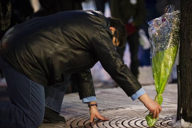 A person places a flower arrangement against a tree during the vigil.