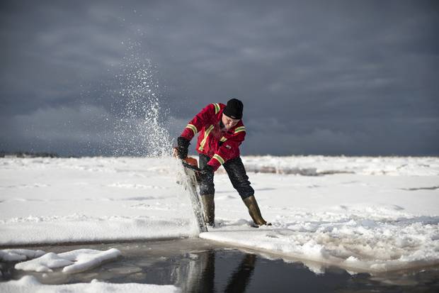 Brian Lewis, co-owner of Future Seafood, cuts through the ice with a chainsaw to look for their oyster trays on Salutation Cove.