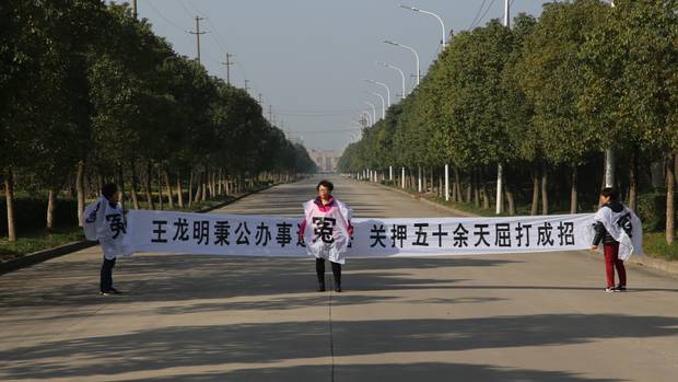 Jean Zou holds a protest banner on a street in Wuhu, China, near where her husband was detained. It reads, in part: ‘Confession under torture after more than 50 days in detention.’