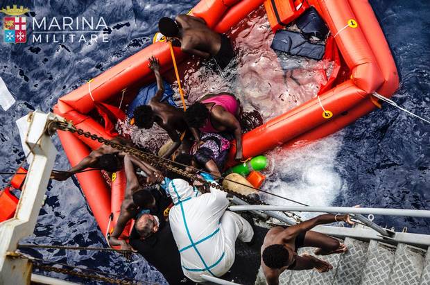 In this photo taken May 27, 2016, in the Mediterranean off the Libyan coast, rescuers help migrants to board the Italian Navy ship Vega after the boat they were aboard sunk.