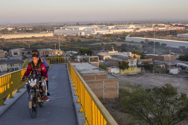 Men on a motorbike, with a Ford assembly plant behind, outside of Irapuato in May of 2017.