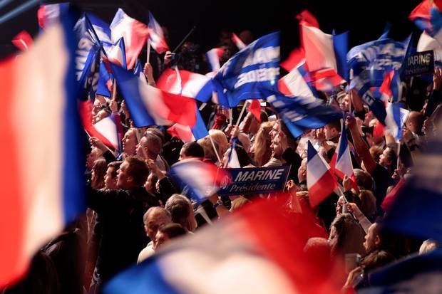 Supporters wave French national flags as they cheer ahead of a Marine Le Pen rally in Paris on April 17, 2017.