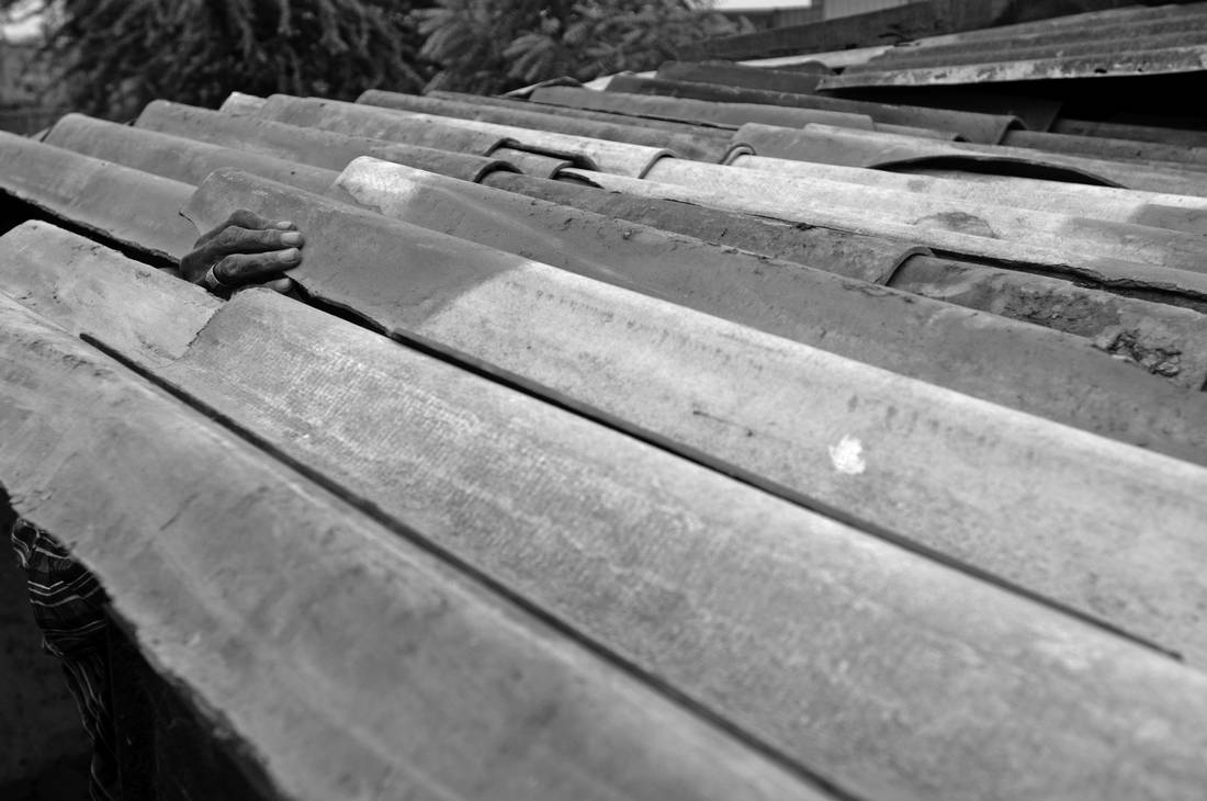 A man working with asbestos cement roof tile adjusts tiles on the roof of a house in a small slum located on the outskirts of Ahmedabad, India. This entire community is built on top of and from the asbestos scraps and dumps from decades of production at the Shree Digvijay Cement Plant. This man broke numerous pieces of roof tile containing asbestos wearing no protection what so ever. Broken sheets of asbestos cement products can release deadly fibres into the air.