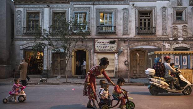 An ethnic Uyghur woman pushes her children on a tricycle in the old town of Kashgar, in the far western Xinjiang province, China on June 28, 2017. 