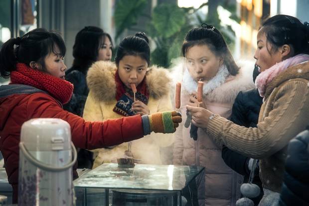 Schoolgirls buy hot dogs on a stick from a street vendor outside a skating rink. Teenaged social life plays out here in much the same way as anywhere, with cliques converging en masse on Pyongyang’s leisure centres and its few department stores every day after school gets out.