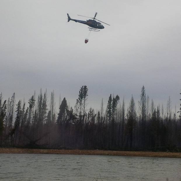 Ken Saumure, a pilot with Phoenix Heli-Flight, fills a bucket with water to douse a hotspot near the company's hangers and fuel tanks.