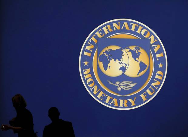 Visitors are silhouetted against the logo of the International Monetary Fund at the main venue for the IMF and World Bank annual meeting in Tokyo, October 10, 2012.