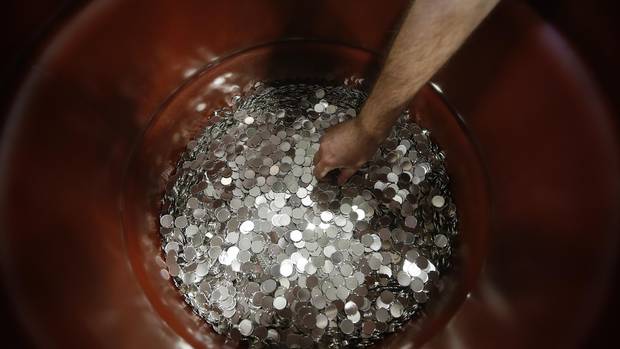An employee reaches into a drum of rejected nickel plated blanks roll along a conveyor belt at the Royal Canadian Mint in Winnipeg Tuesday, April 4, 2017.