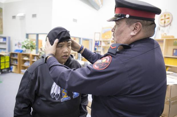 Senior Constable Brice Iron Shirt, the school resource officer in Stand Off, Alta., helps fit a new hat on student cadet, Felix Many Bears. The local police department has a student recruitment program for teens who can join the cadet program to learn about local policing and community concerns.