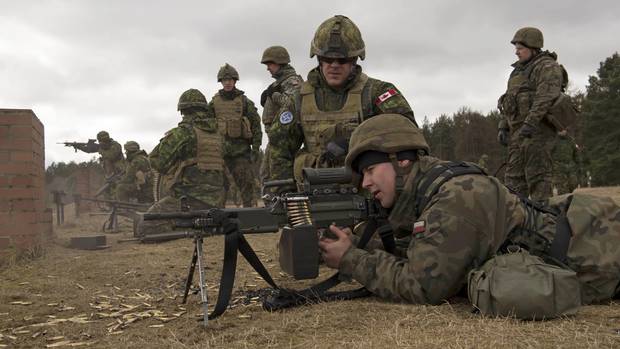 A Canadian Armed Forces member looks on as a Polish soldier fires a C9 machine gun at a training area in Poland March 15, 2016.