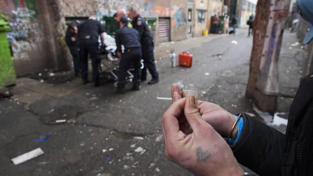 A drug user prepares a hit as first responders help an overdose victim in an alley in Vancouver’s Downtown Eastside.