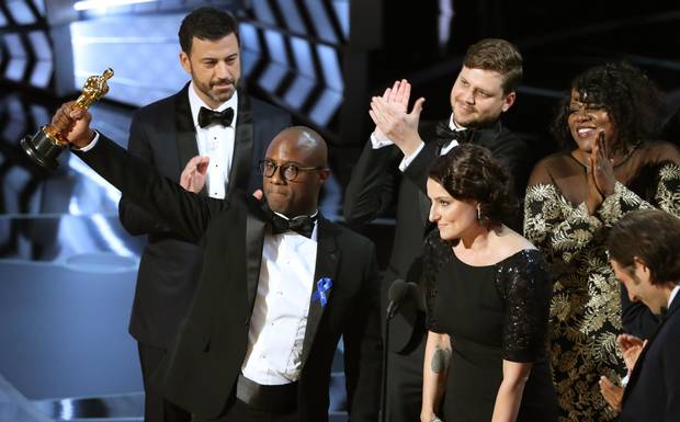 Barry Jenkins, writer and director of Moonlight, holds up the Best Picture Oscar in front of host Jimmy Kimmel (rear) as he stands with Producer Adele Romanski.