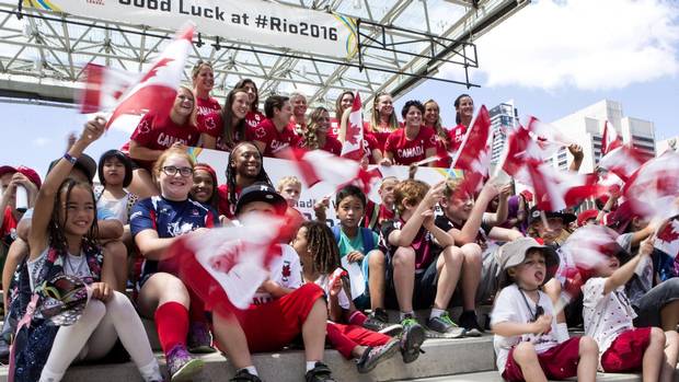 Members of Canada's Women's Rugby Sevens team pose for a photo with flag-waving children at an event ahead of the Rio Games.