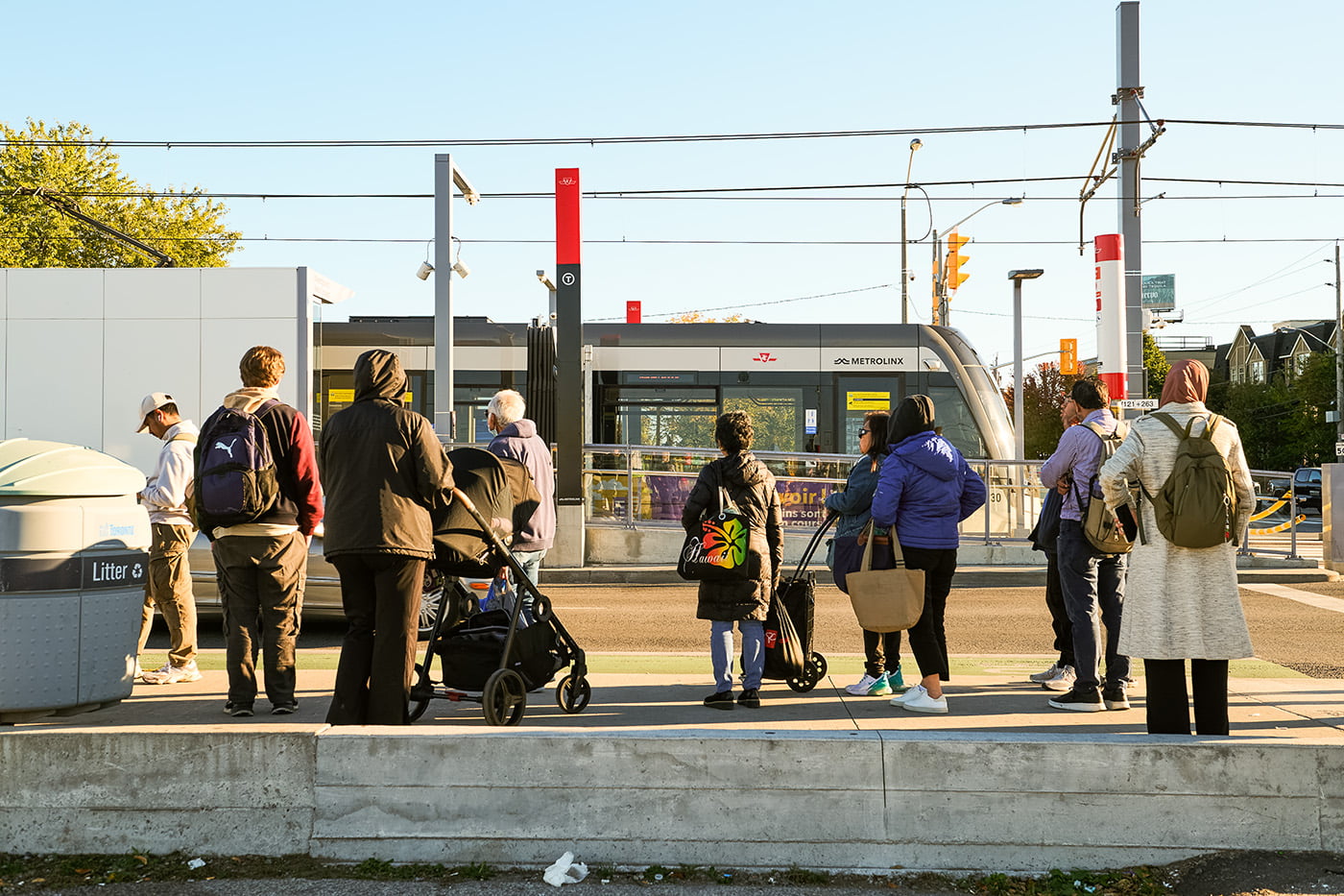 Members of the public queue for a bus along Eglinton Avenue, with a test train visible in the background that will eventually carry passengers as part of the Eglinton Crosstown LRT in Toronto, Oct. 9, 2025. The trains are part of the system’s ongoing testing phase ahead of the line’s eventual opening.