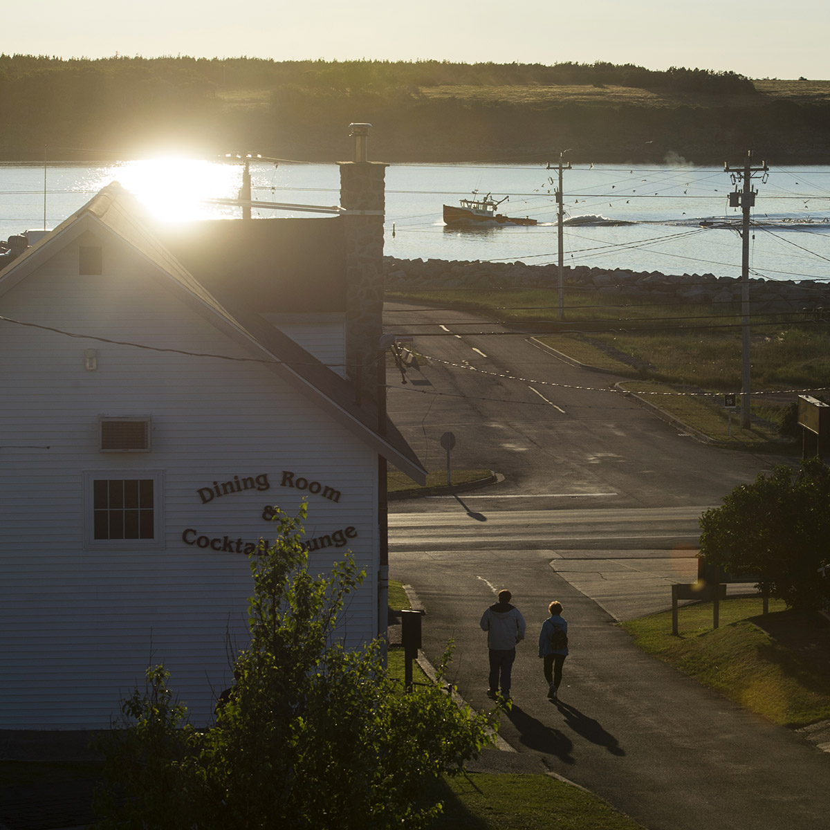 Locals walk down a laneway as a fishing boat pulls into Cheticamp Harbour in Cheticamp, N.S., an Acadian fishing community on Cape Breton Island, at dusk July 13, 2017.