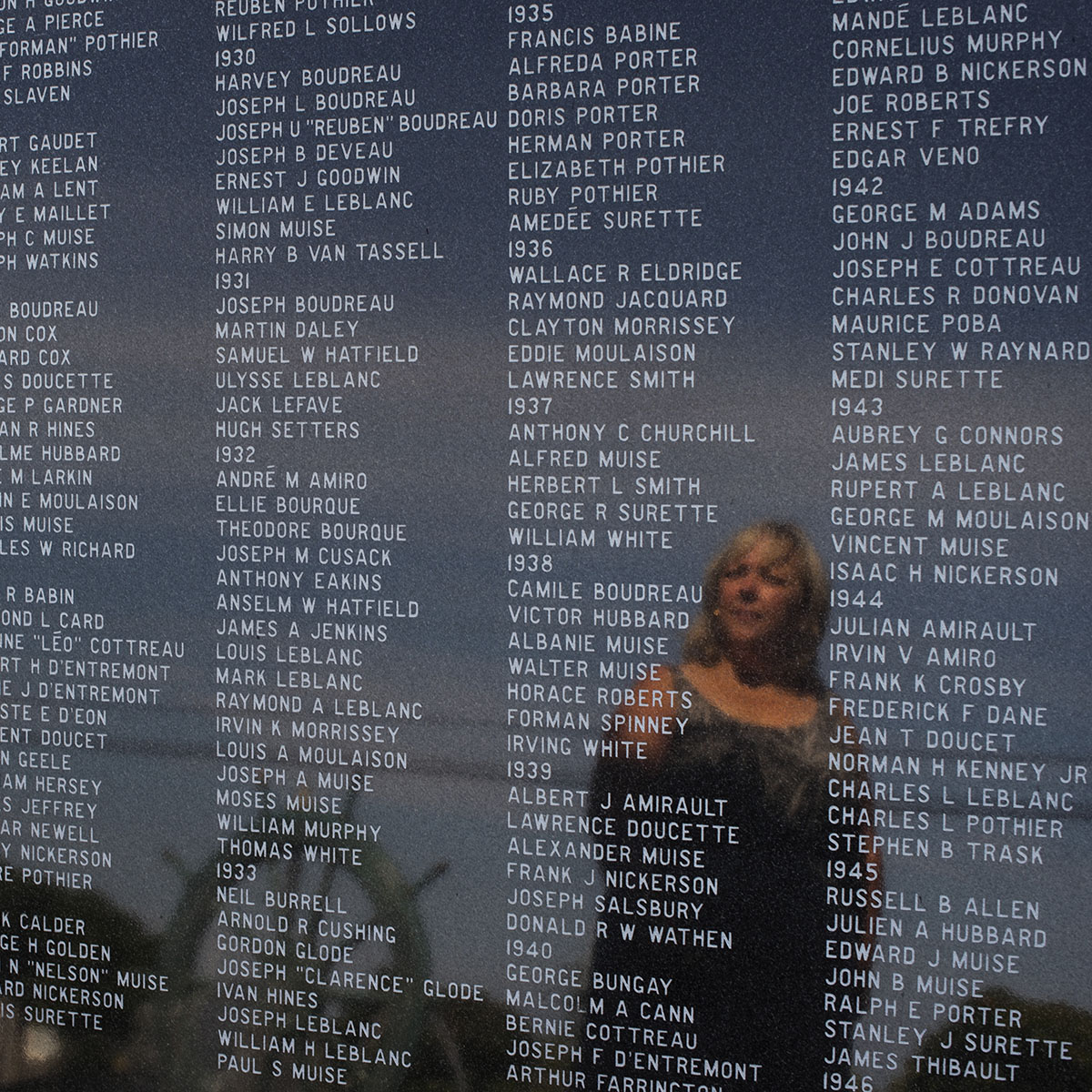 Widow Marilyn D'Entremont is reflected in the memorial for those 'Lost to the Sea' where her grandfather's and husband's names are among the thousands etched on the monument in Yarmouth, N.S.