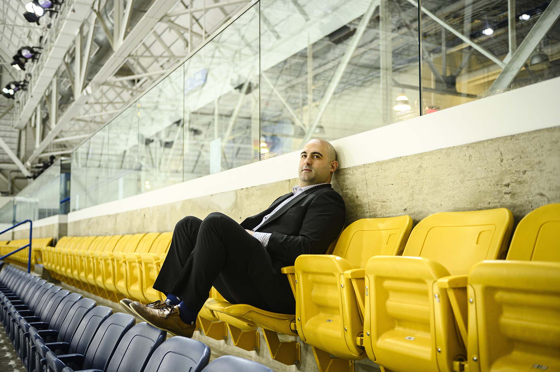 Mark DeMontis poses for a photograph seated in a row of yellow chairs in the stands at the Carnegie Cup elite Blind Hockey Series in Toronto.
