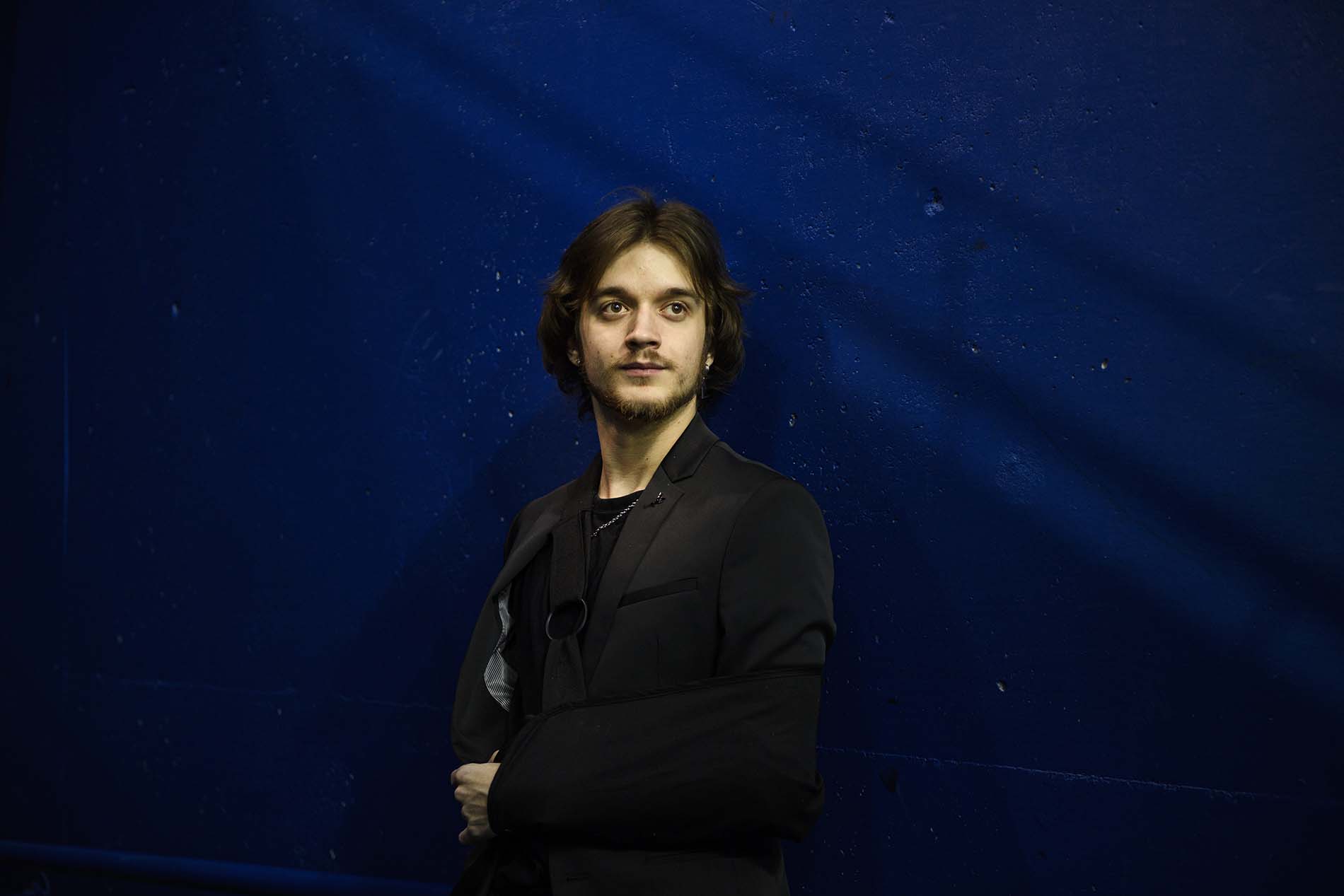 Joe Fornasier, wearing a black suit with his arm in a sling, poses for a photograph against a blue backdrop.