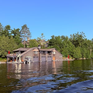 On July 17, 2026 one of Canada’s most extraordinary private estates became the backdrop for one of the country’s most influential gatherings. Prime Minister Mark Carney was in Muskoka for the invitation-only Dock (un)Conference, hosted at Ferndale, the Lake Rosseau estate of Peter Gilgan, founder of Mattamy Homes. Bringing together leaders in business, technology and government, the conference is designed to encourage open discussions about Canada’s future in a private setting.
Cruising by two of the five boathouses on the Ferndale property on Lake Rosseau. At one time this magnificent property was called Ferndale House (a grand resort) and later it was sold to a Christian organization called the Canadian Keswick Conference Centre. It burned down in 1946. The property now supports five boathouses along with a massive cottage, guesthouse, sandy beach, sports courts and a helicopter pad. The property is owned by a self made Canadian Billionaire who has amassed great success in the home building business. July 24, 2026
On July 17, 2026 one of Canada’s most extraordinary private estates became the backdrop for one of the country’s most influential gatherings. Prime Minister Mark Carney was in Muskoka for the invitation-only Dock (un)Conference, hosted at Ferndale, the Lake Rosseau estate of Peter Gilgan, founder of Mattamy Homes. Bringing together leaders in business, technology and government, the conference is designed to encourage open discussions about Canada’s future in a private setting.
Cruising by two of the five boathouses on the Ferndale property on Lake Rosseau. At one time this magnificent property was called Ferndale House (a grand resort) and later it was sold to a Christian organization called the Canadian Keswick Conference Centre. It burned down in 1946. The property now supports five boathouses along with a massive cottage, guesthouse, sandy beach, sports courts and a helicopter pad. The property is owned by a self made Canadian Billiona