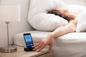 Woman Turning Off The Alarm On Cell Phone While Waking Up In The Morning