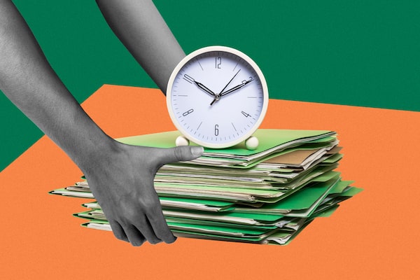 Hands hold a stack of papers and folders with a small clock sitting on top.