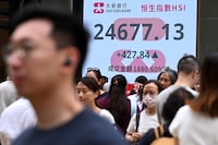 Pedestrians walk across a street next to an electronic sign board showing the Hang Seng Index in Hong Kong on June 12, 2026. (Photo by Peter PARKS / AFP via Getty Images)