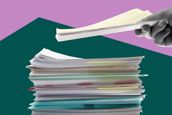 A hand puts more papers on top of a tall stack of paperwork.