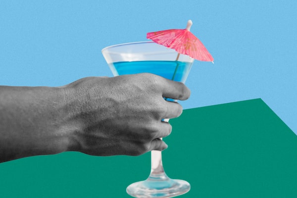 A hand holds a drink with a pink cocktail umbrella sticking out the top.