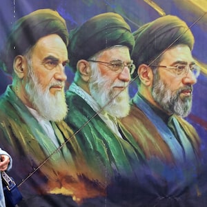 A woman walks past a banner featuring Iran's late supreme leaders Ayatollah Ruhollah Khomeini (L) and Ayatollah Ali Khamenei (C) next to newly elected supreme leader Ayatollah Mojtaba Khamenei, in Tehran on April 19, 2026. The strategic Strait of Hormuz was again closed on April 19 in the stand-off between Iran and the United States, with Iran's powerful parliament speaker signalling a final peace deal remained "far" off despite some movement in negotiations. (Photo by ATTA KENARE / AFP via Getty Images) /