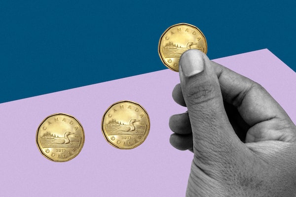 A hand holds up one loonie out of a group of three.