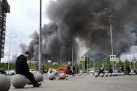People are seen outside a shopping mall as black smoke rises from the area of the Russian oil producer Gazprom Neft's Moscow oil refinery on the south-eastern outskirts of Moscow on June 18, 2026. Moscow was fending off a "large-scale" drone attack from Ukraine, with several drones reaching an oil refinery, the city's mayor Sergey Sobyanin said early on June 18, 2026. (Photo by AFP via Getty Images)