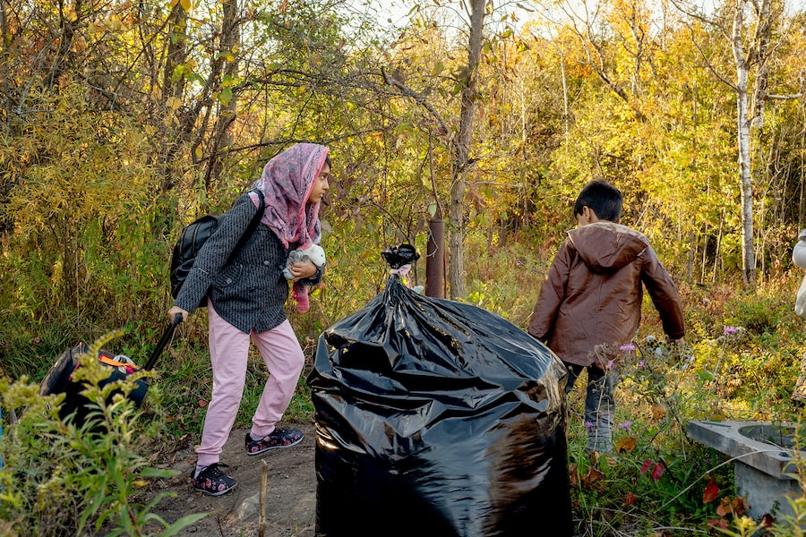 A family pulls their belongings from the U.S. side of the Roxham Road border site to the Canadian side, via a path and across a dry ditch. Whatever they wish to bring into Canada must accompany them in one go, so kids often help carry things. 