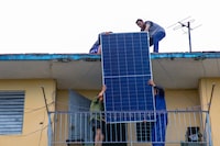Installers lift a solar panel onto the rooftop of a multi-family building in Matanzas, Cuba, on Monday.