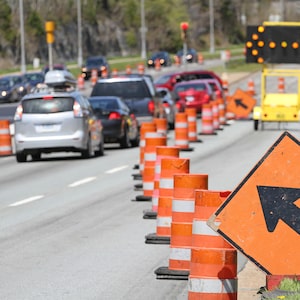 A standard move left sign and a digital flashing arrow with traffic cones advises all traffic to move into the left lane. Shot shallow dof with focus on foreground arrow sign.