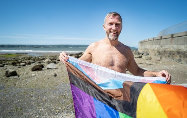 Sean Fitzgerald, co-president of the Federation of Gay Games, waves a Progress Pride flag as he stands on Second Beach along the Stanley Park seawall, in Vancouver, B.C. on Monday, June 5, 2023. Fitzgerald competes in water polo and swimming at the Gay Games.