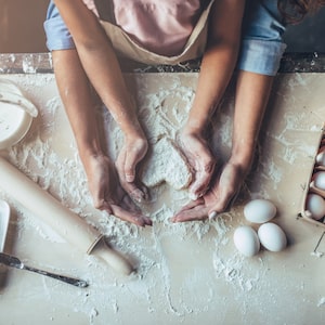 Cropped image of attractive young woman and her little cute daughter are cooking on kitchen. Having fun together while making cakes and cookies. Top view of mom with daughter making dough heart.