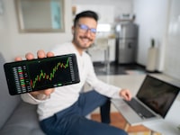 Happy Latin American man at home looking at his investments in the stock market on his cell phone