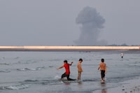 Three boys play in the shallow waters of the Strait of Hormuz, as a plume of smoke rises from an explosion in the background, off Bandar Abbas, Iran, on July 13.
